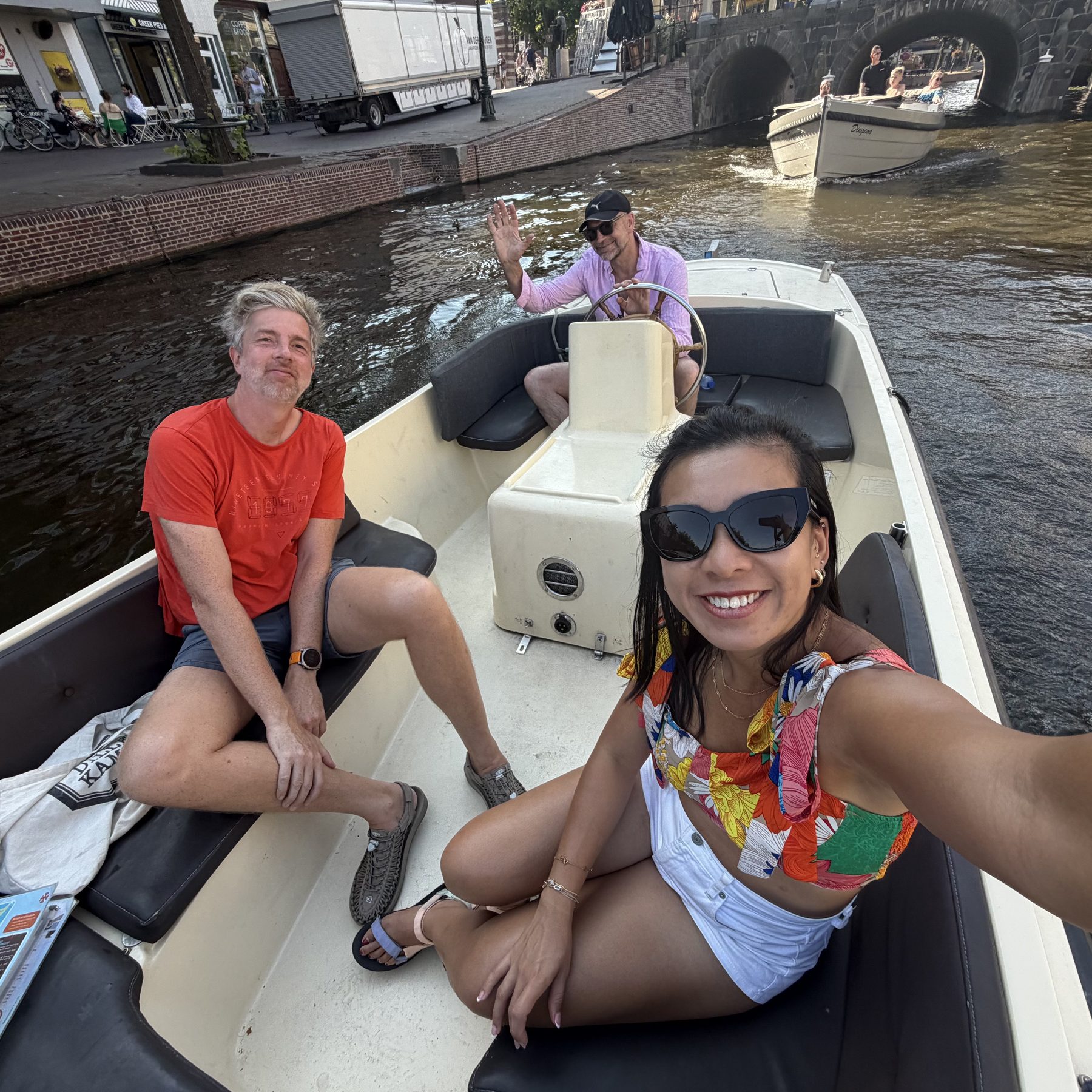 Selfie chaos: Cristyne driving the camera, Alex in the orange tee, friend waving from the helm like we invented summer.