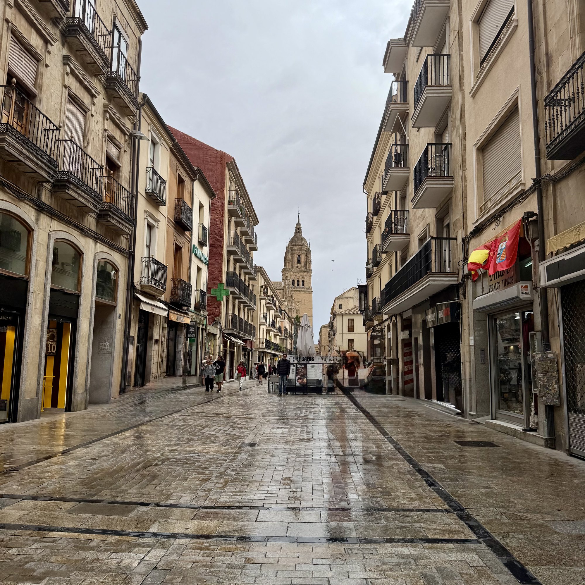 Wet stone, grey sky, and the cathedral parked at the end of the street like it owns the vanishing point. Summer clothes, 21°C. The math is not mathing.